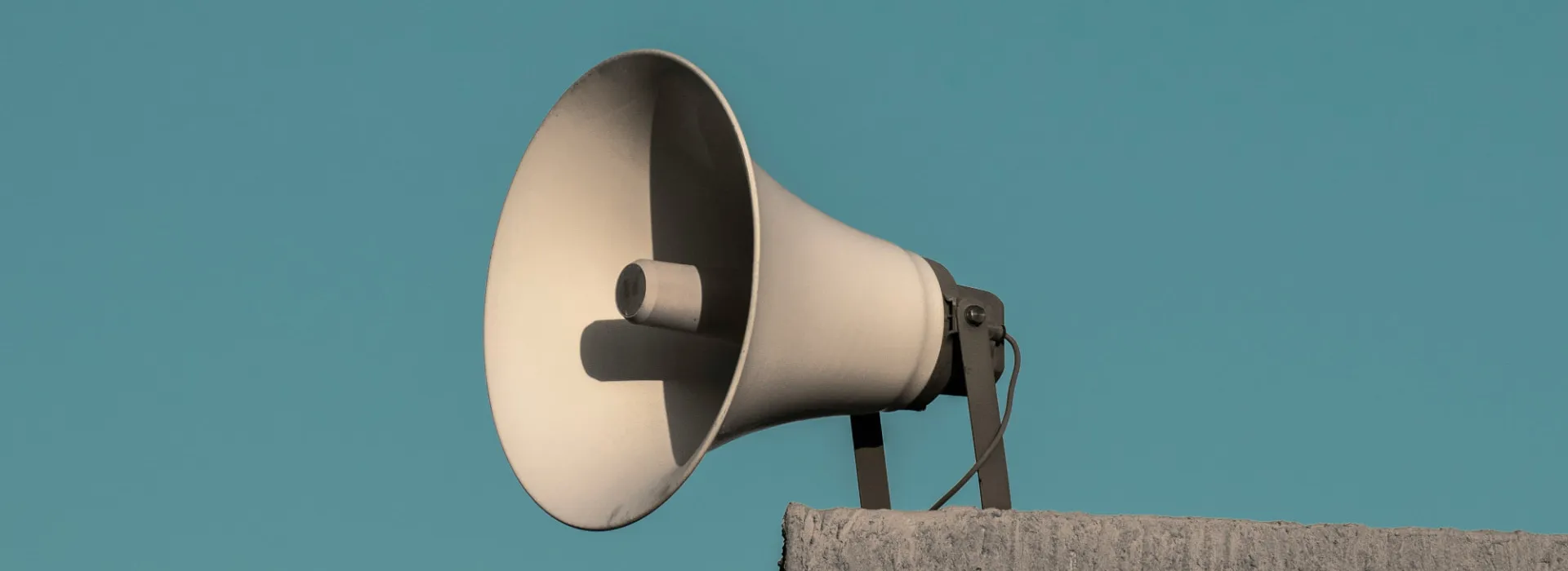 Loudspeaker mounted on a concrete wall against a clear blue sky